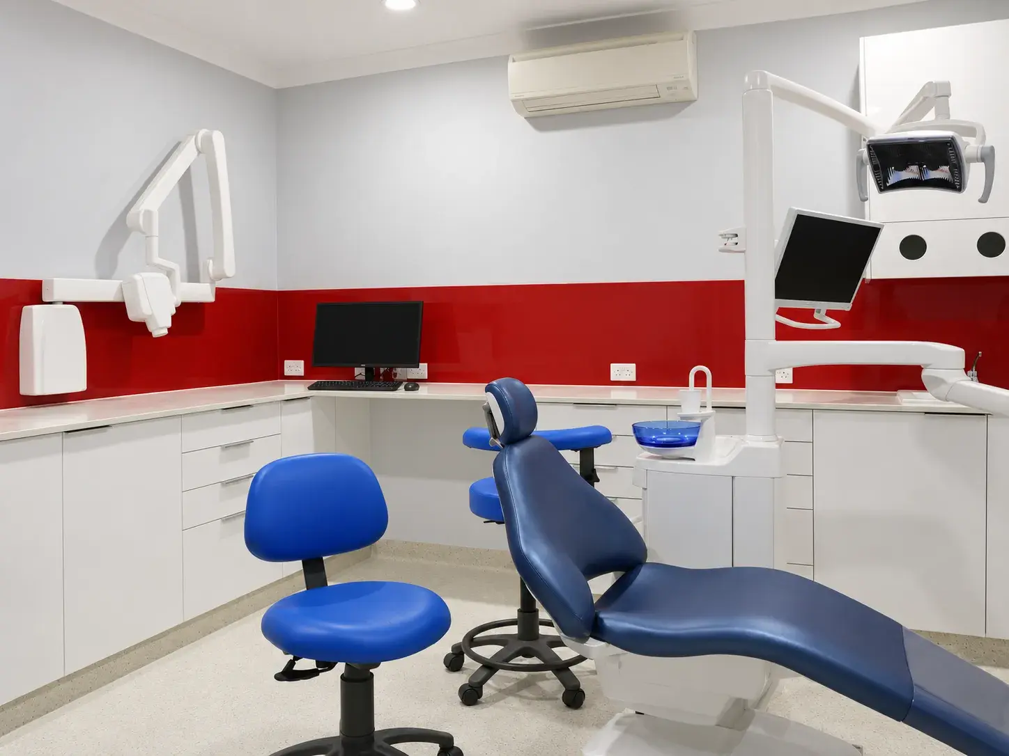 Our treatment room, with a navy dental chair in front of a red splashback